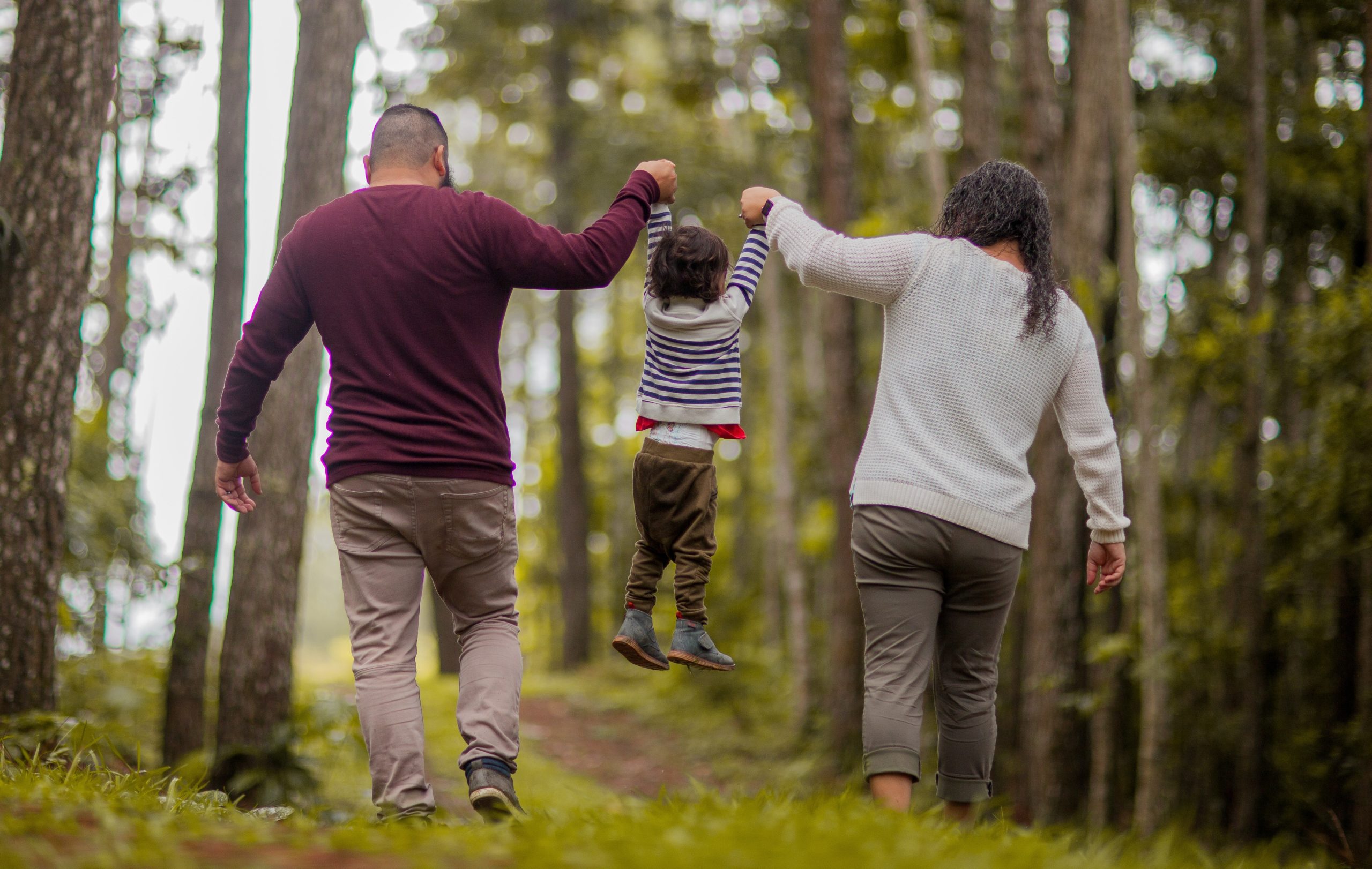 Mom, baby, and dad walking in a forest.